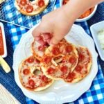 Hand reaching down onto a plate of air fryer mini pizza dinner