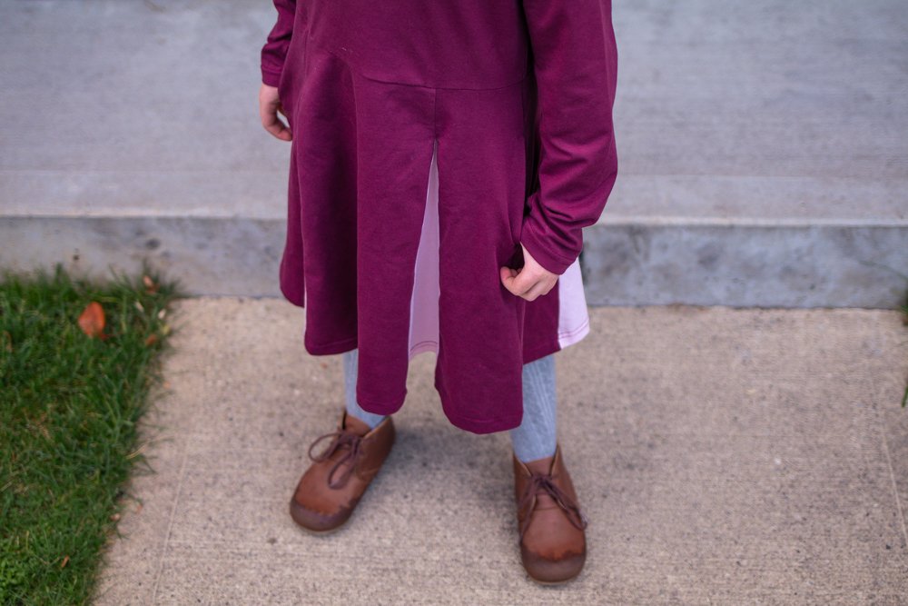 downward view of child wearing purple skater dress and brown boots