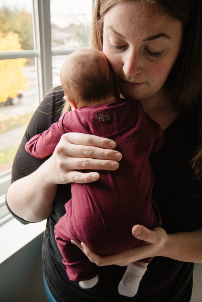 mom holding baby near a window wearing a onesie