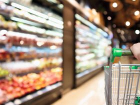 woman hand hold supermarket shopping cart with abstract blur organic fresh fruits and vegetable on shelves in grocery store defocused bokeh light background